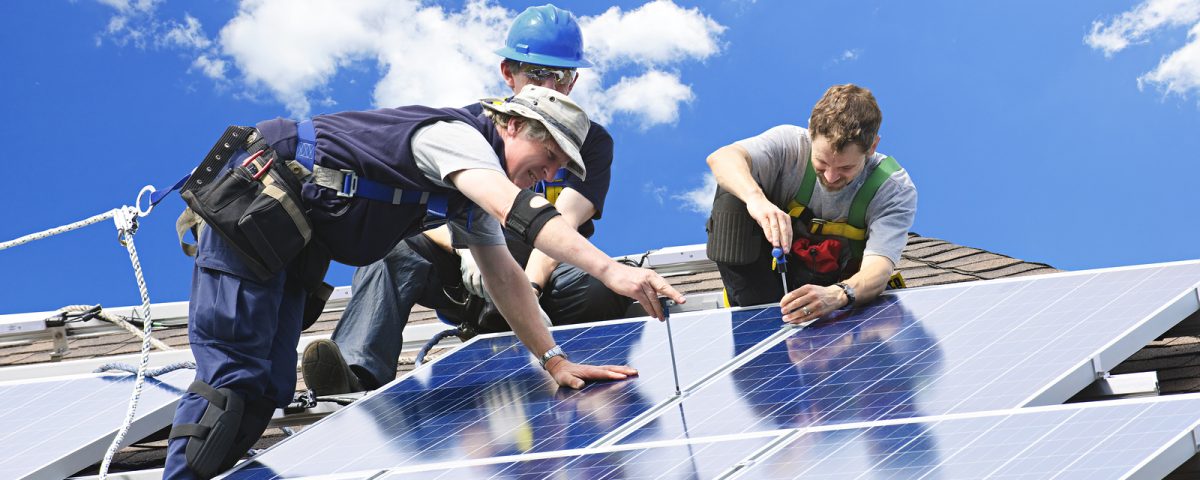 Workers installing alternative energy photo-voltaic solar panels on roof